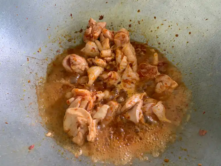 Chicken pieces cooking and absorbing the curry paste flavor.
