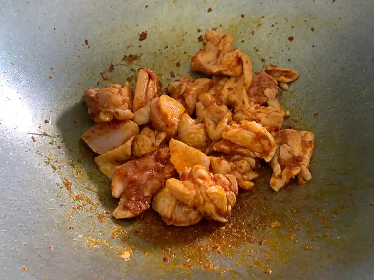 Sliced chicken added to fried Panang curry paste in a wok.