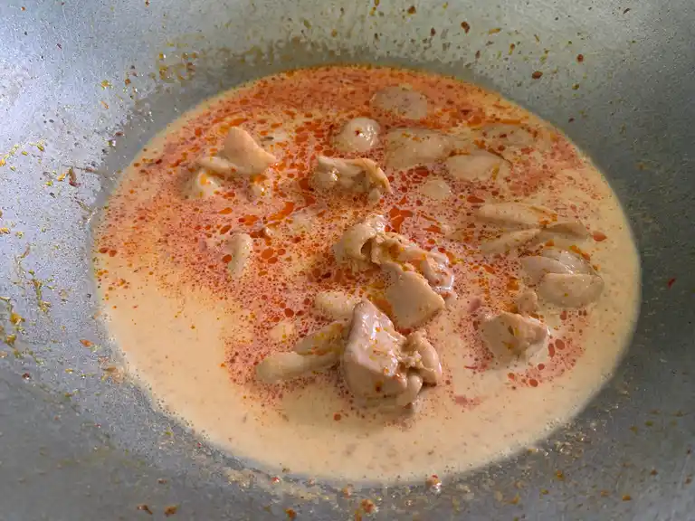 Coconut milk poured into the wok with chicken and curry paste.