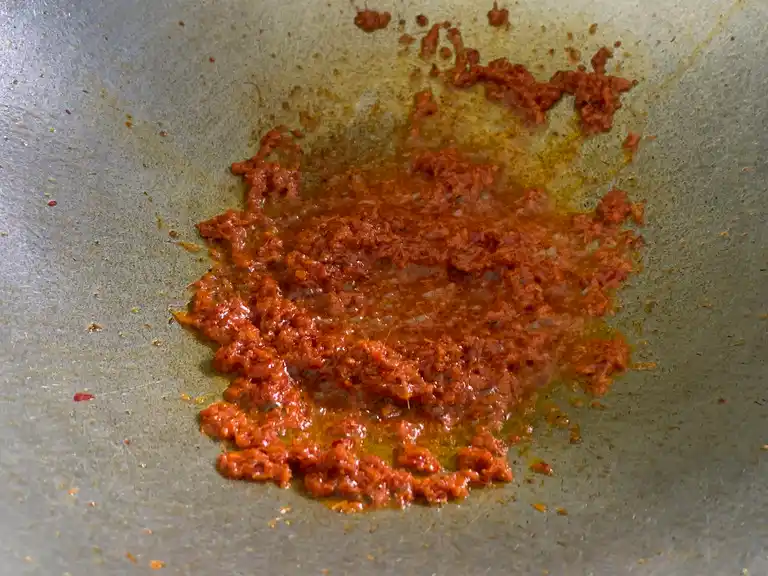 Panang curry paste being fried in oil until fragrant in a wok.
