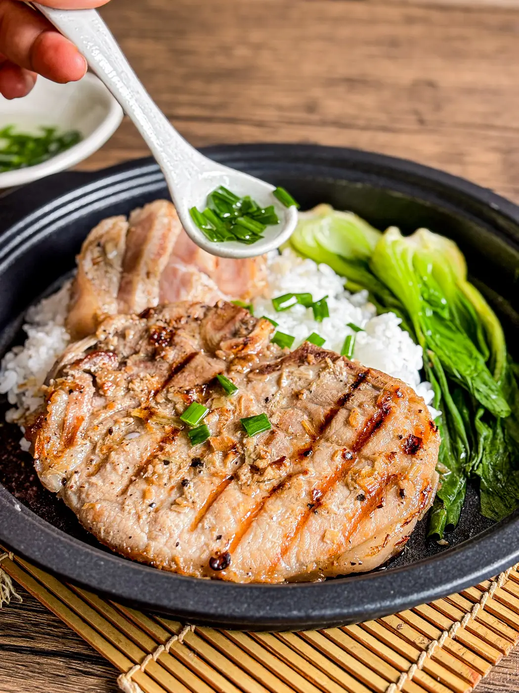 Vietnamese grilled pork chop served with steamed rice, bok choy, and a spoonful of scallion oil garnish.