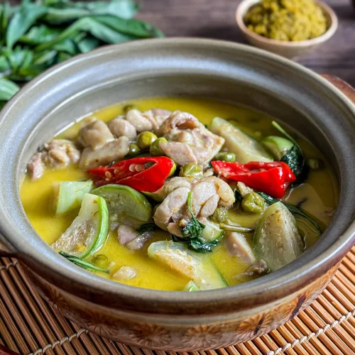 Authentic Thai green curry chicken with vegetables, coconut milk, and chilies served in a clay pot, with fresh basil and curry paste in the background.
