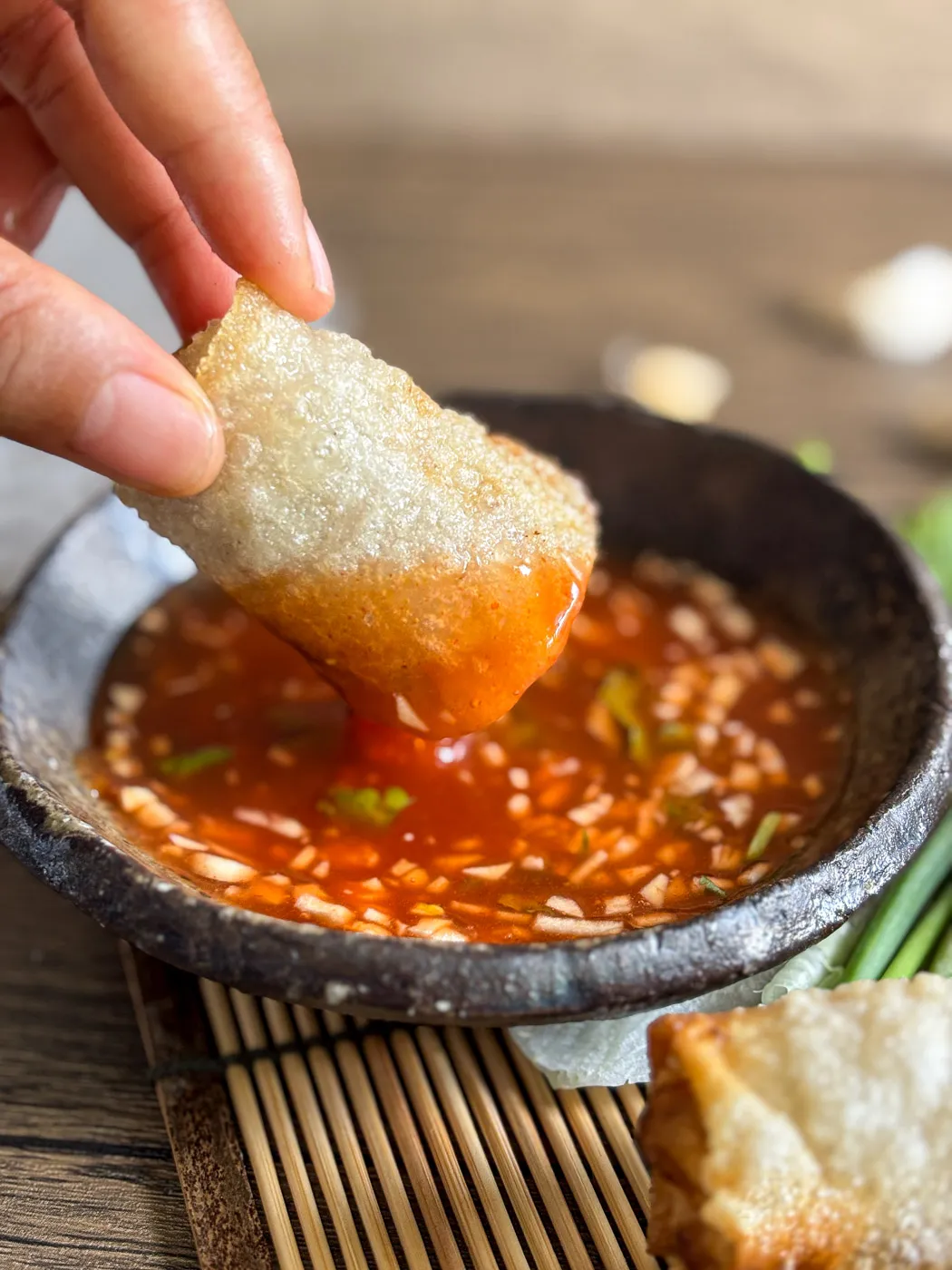 Vietnamese fried spring roll (chả giò) being dipped in garlic chili dipping sauce.