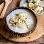Vietnamese chè chuối dessert in a wooden bowl, with bananas, tapioca pearls, coconut milk, and a topping of crushed roasted peanuts.