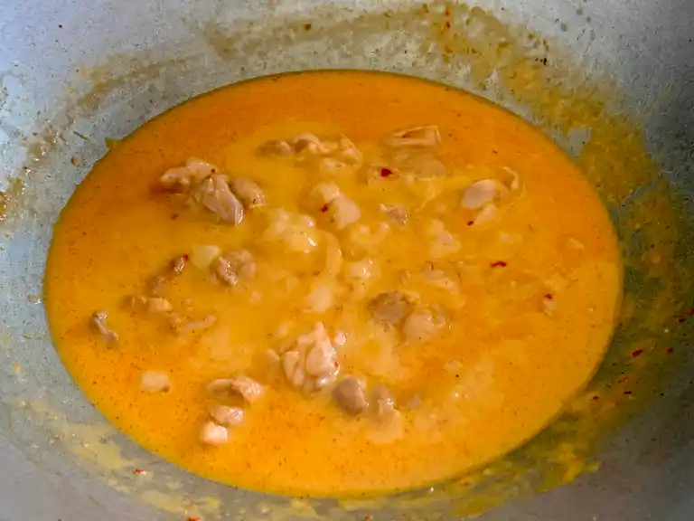 Thai red curry sauce thickening around tender chicken pieces.