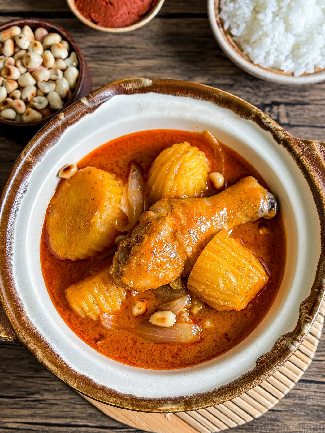 Thai chicken massaman curry with drumstick, crinkle-cut potatoes, roasted peanuts, and onions in a clay bowl, served with jasmine rice.