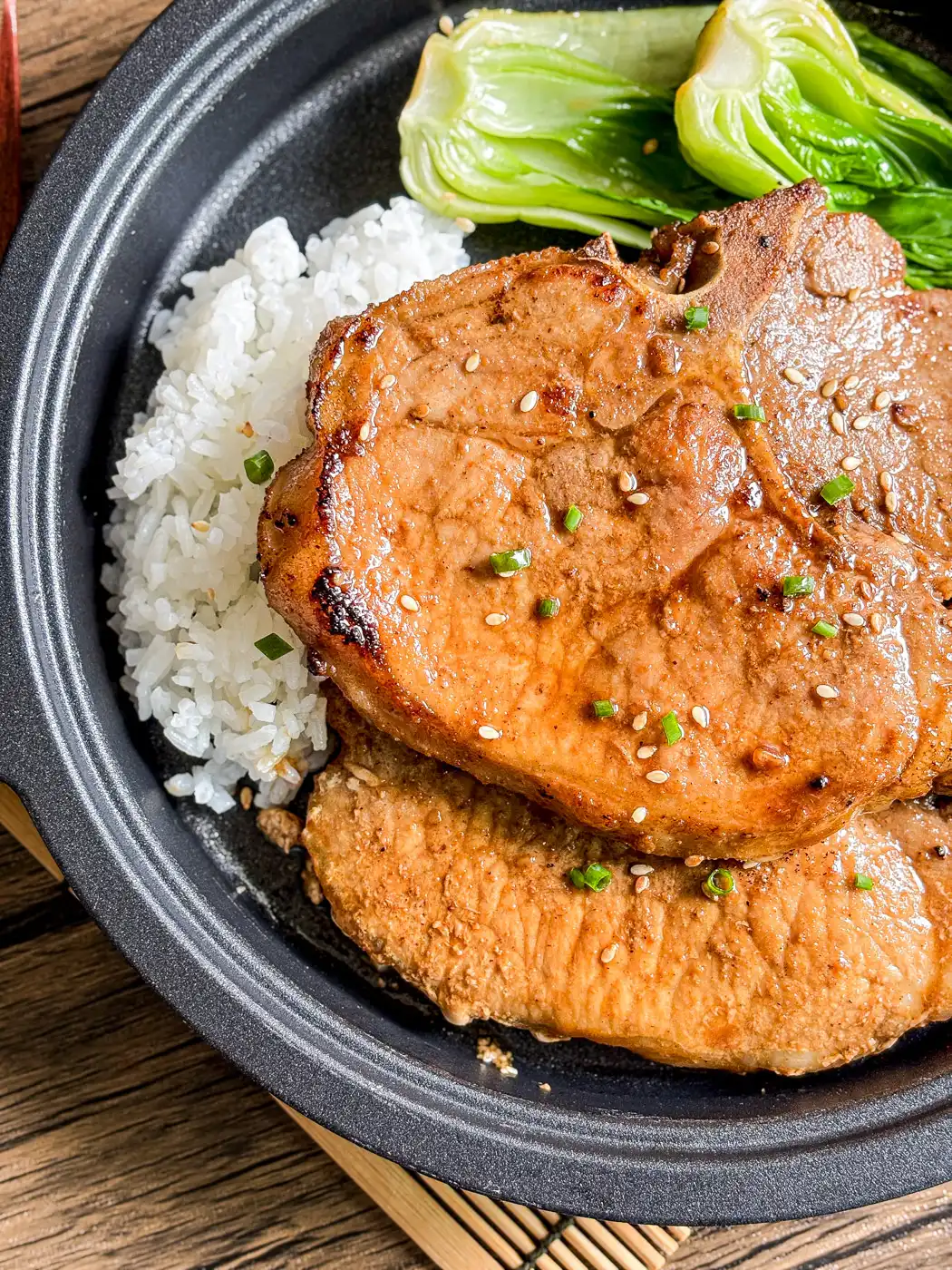 Close-up of grilled hoisin pork chops served with steamed rice and baby bok choy, garnished with sesame seeds and green onions.