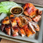 Thai grilled lemongrass chicken sliced and served with dipping sauce and lettuce on a ceramic plate.