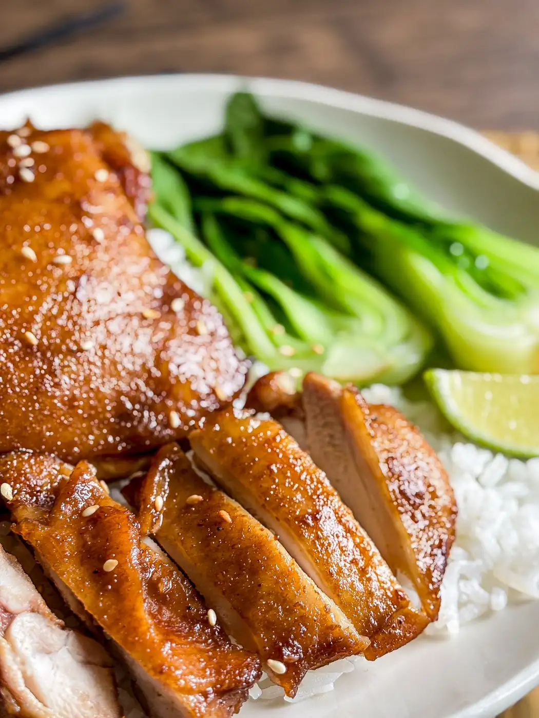 Close-up of juicy hoisin chicken thighs sliced over white rice with steamed bok choy and lime.