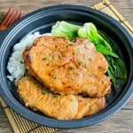 Hoisin pork chops with white rice and bok choy, ready to eat on a bamboo placemat.