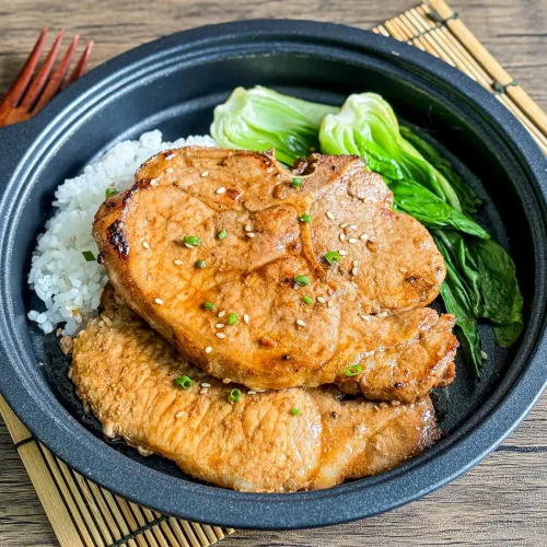 Hoisin pork chops with white rice and bok choy, ready to eat on a bamboo placemat.