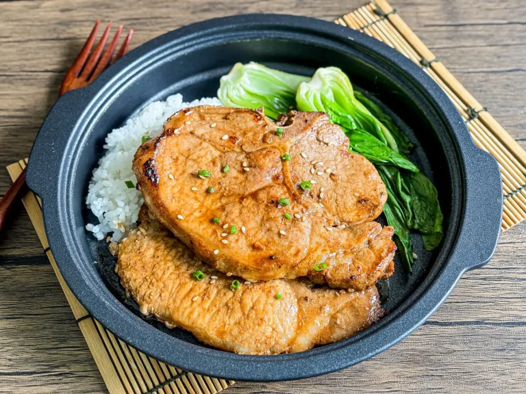 Hoisin pork chops with white rice and bok choy, ready to eat on a bamboo placemat.