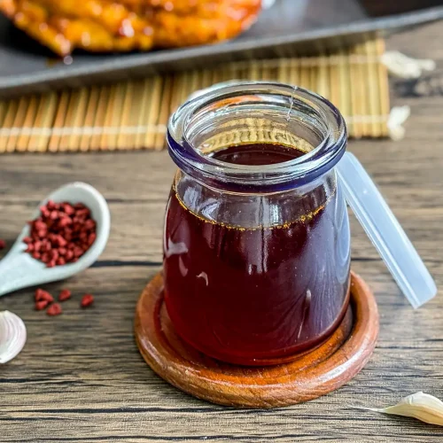 Jar of homemade inasal chicken oil with annatto seeds and garlic on a wooden table.