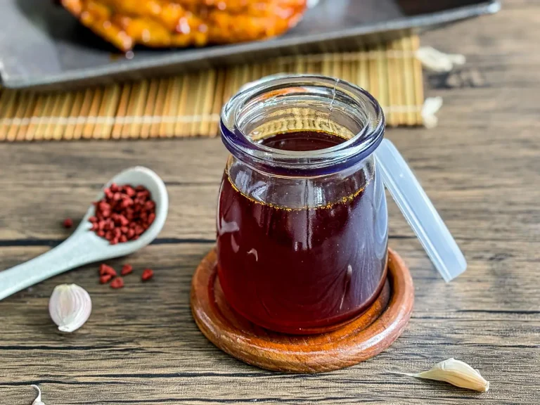 Jar of homemade inasal chicken oil with annatto seeds and garlic on a wooden table.