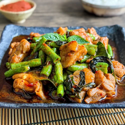 Pad prik gaeng gai, a Thai chicken red curry stir-fry with vegetables served on a dark ceramic plate with jasmine rice in the background.