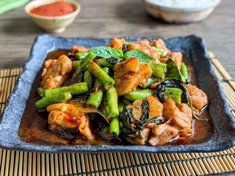 Pad prik gaeng gai, a Thai chicken red curry stir-fry with vegetables served on a dark ceramic plate with jasmine rice in the background.