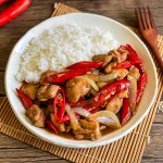 Pad prik gai served with steamed jasmine rice, featuring stir-fried chicken with red chilies and onions in a savory sauce.