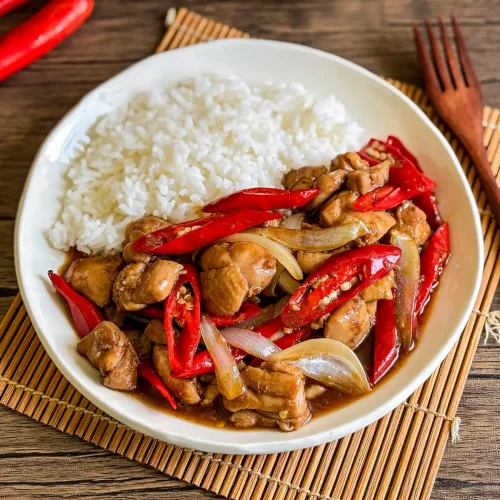 Pad prik gai served with steamed jasmine rice, featuring stir-fried chicken with red chilies and onions in a savory sauce.