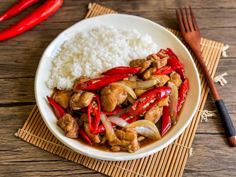 Pad prik gai served with steamed jasmine rice, featuring stir-fried chicken with red chilies and onions in a savory sauce.