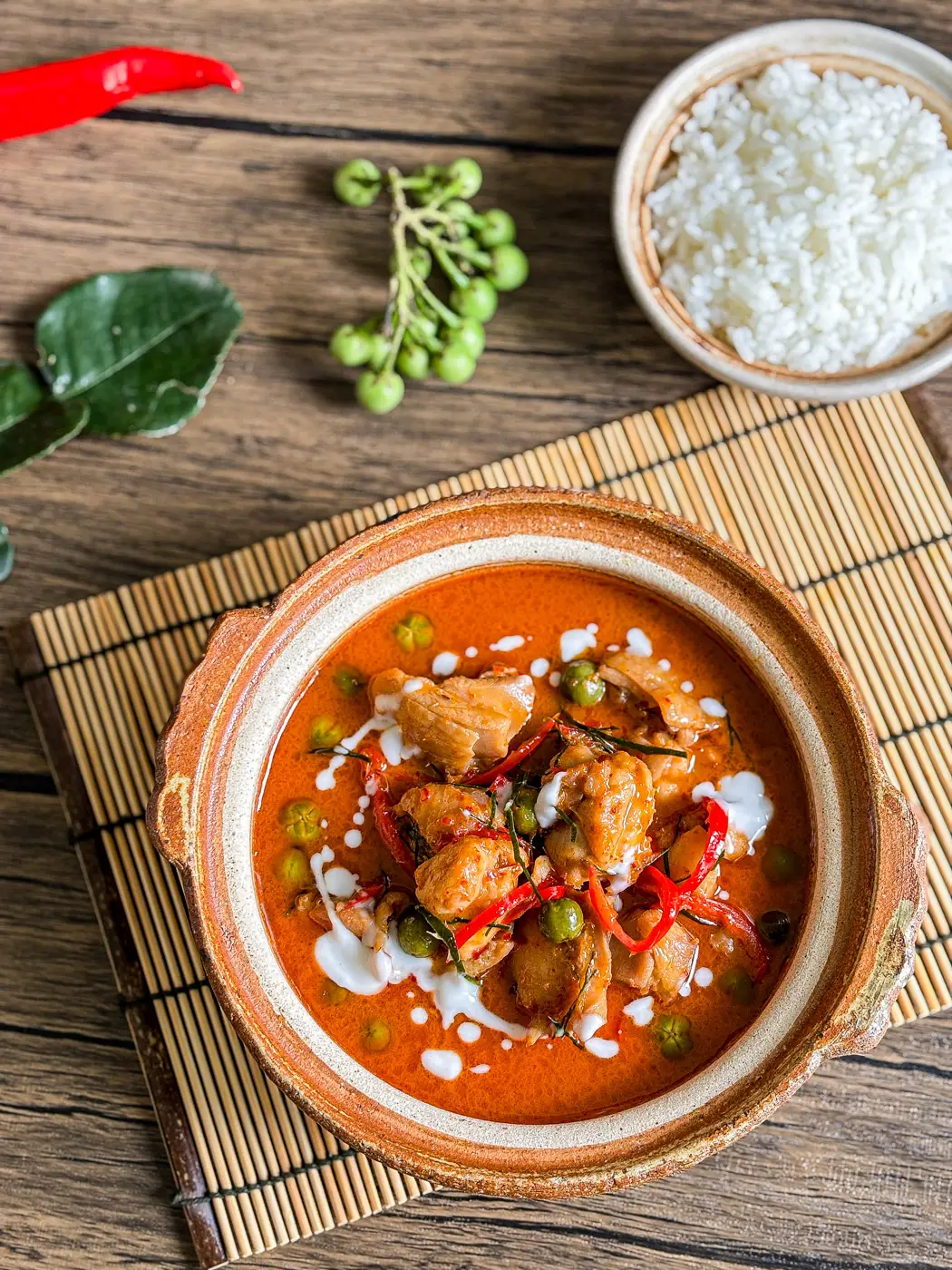 Overhead view of Thai panang curry with chicken, pea eggplants, red chilies, and coconut milk, served with jasmine rice.