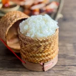 Thai sticky rice served in a traditional woven bamboo basket on a wooden table.
