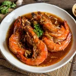 Thai garlic shrimp served on a white plate, topped with crispy garlic and garnished with fresh cilantro.