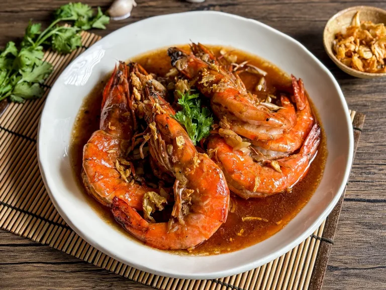 Thai garlic shrimp served on a white plate, topped with crispy garlic and garnished with fresh cilantro.
