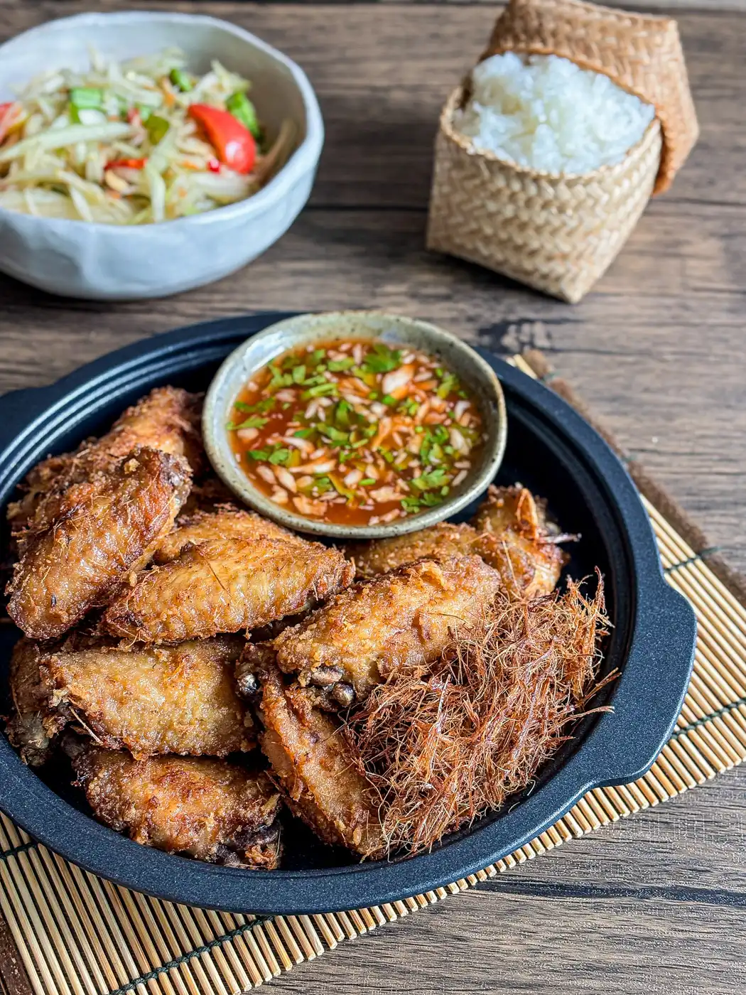 Thai lemongrass fried chicken wings served with sticky rice and papaya salad, featuring a flavorful dipping sauce in the center.