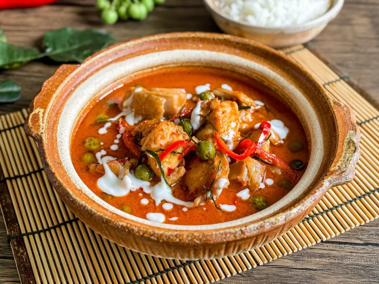 Panang curry with chicken, served in a clay bowl and topped with coconut cream, Thai red chili, and kaffir lime leaves.