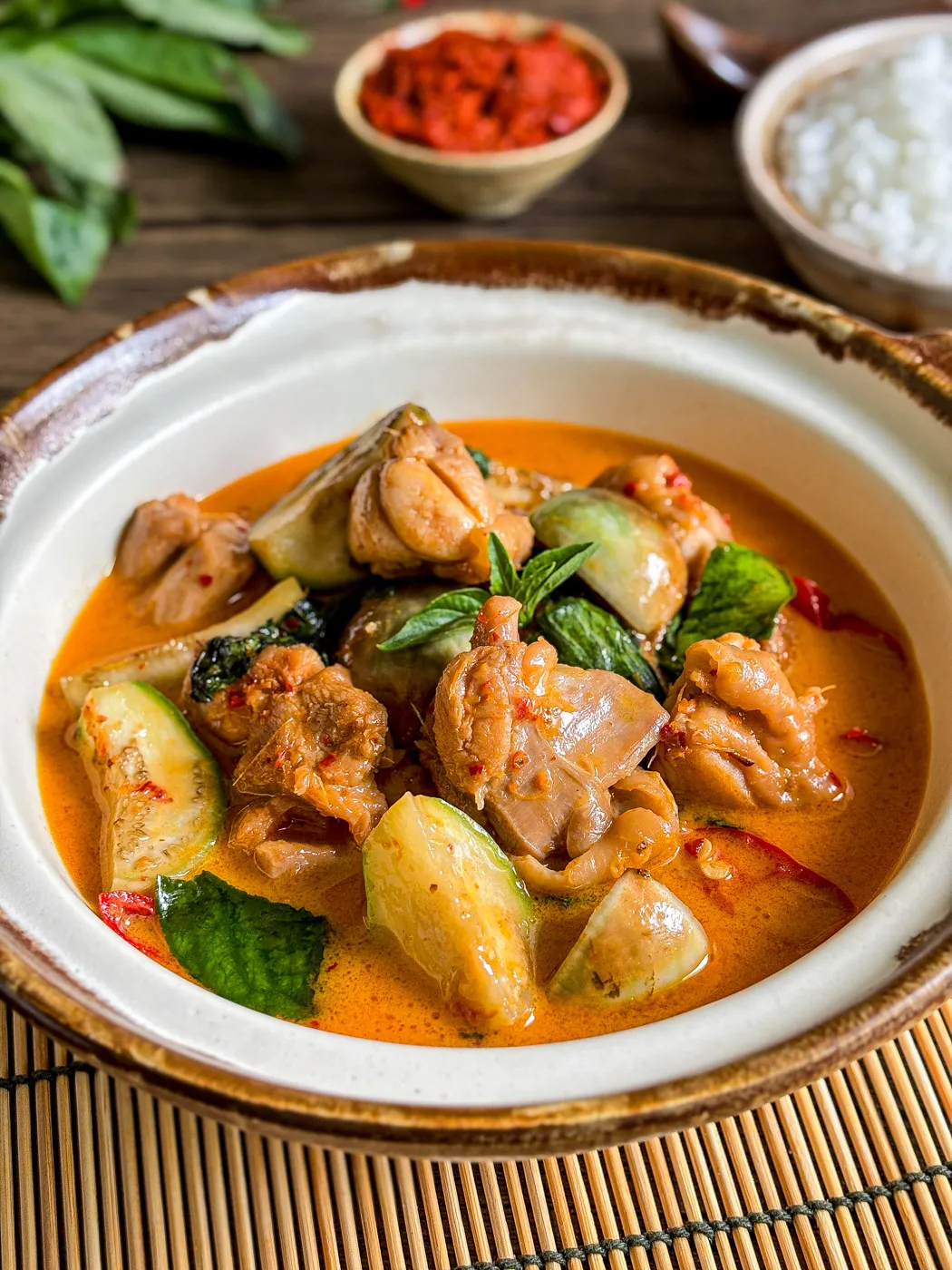 Thai red curry chicken with vegetables and coconut milk, served in a ceramic bowl with visible basil leaves and chilies.