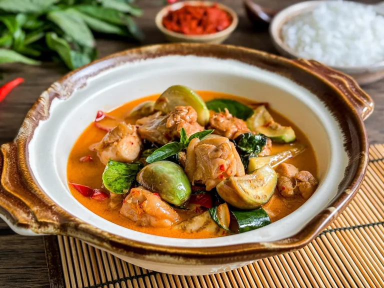 Thai red curry chicken with coconut milk and vegetables served in a rustic ceramic bowl, with rice in the background.