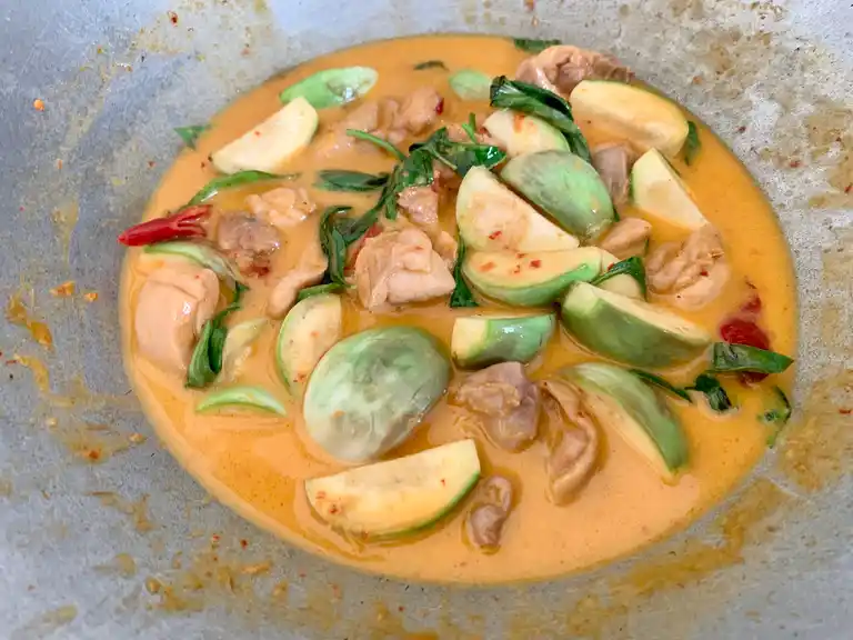Thai red curry with chicken, eggplant, basil leaves, and coconut milk in a wok.