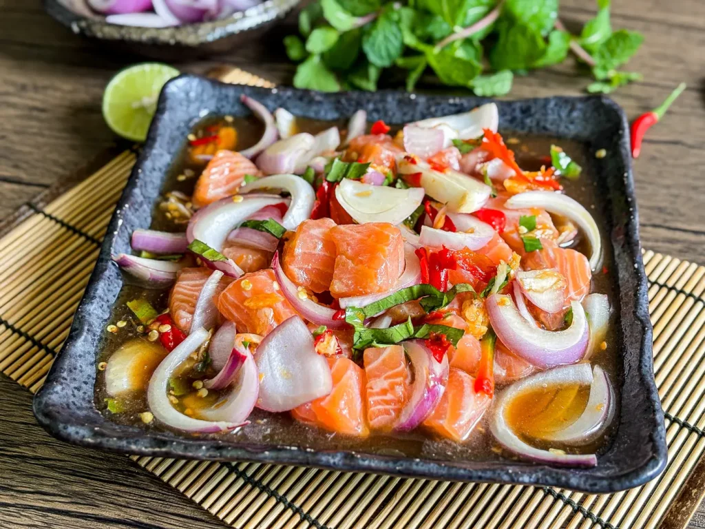 Thai salmon salad with red onions, mint, and lime served on a black square plate.