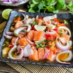 Thai salmon salad with red onions, mint, and lime served on a black square plate.