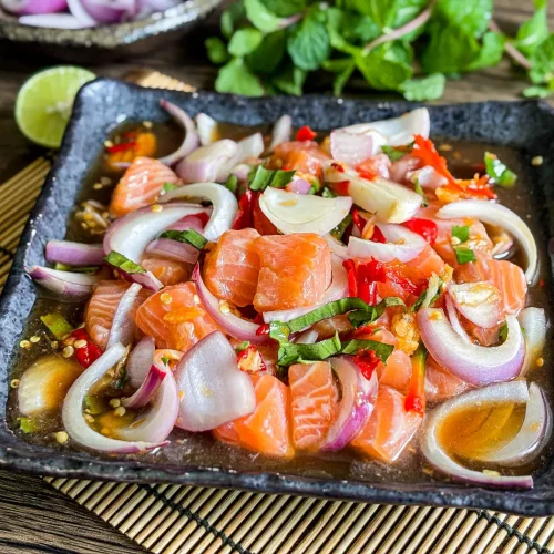 Thai salmon salad with red onions, mint, and lime served on a black square plate.