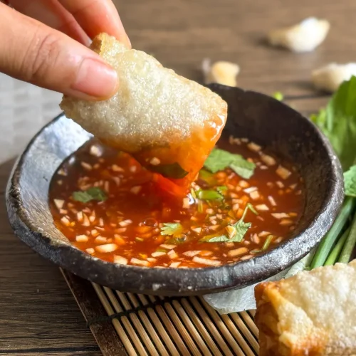 Thai sweet chili garlic sauce is being used as a dip for spring rolls, garnished with fresh herbs.