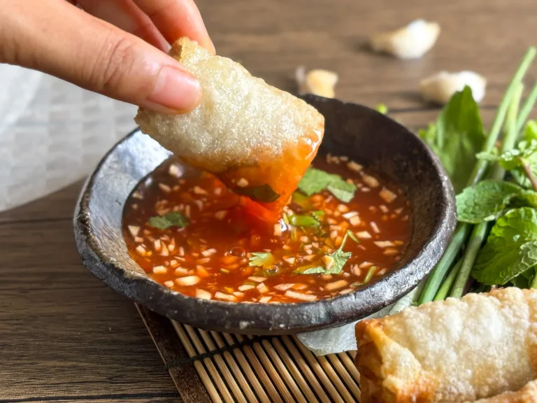 Thai sweet chili garlic sauce is being used as a dip for spring rolls, garnished with fresh herbs.
