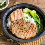 Vietnamese lemongrass pork chops, topped with chopped green onions oil, with a side of rice and fresh vegetables.