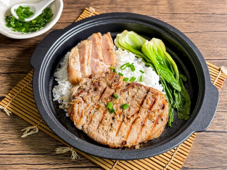 Vietnamese lemongrass pork chops, topped with chopped green onions oil, with a side of rice and fresh vegetables.