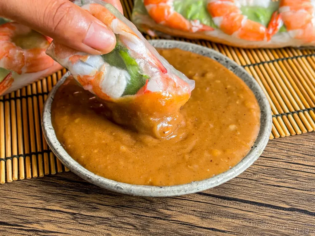 Vietnamese peanut hoisin sauce served with shrimp spring rolls on a bamboo mat.