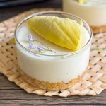No bake durian cheesecake served in glass cups with a cookie crust and fresh durian topping, placed on a woven mat.