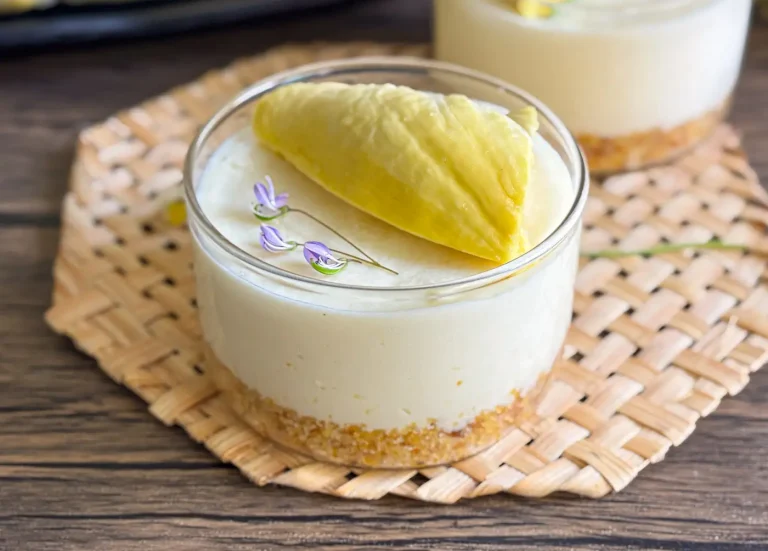No bake durian cheesecake served in glass cups with a cookie crust and fresh durian topping, placed on a woven mat.