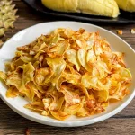 Durian chips fried golden brown served with fresh durian pods on black tray.
