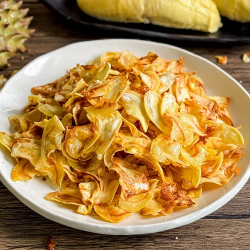 Durian chips fried golden brown served with fresh durian pods on black tray.