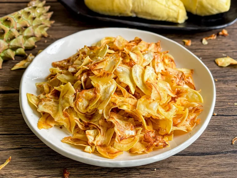 Durian chips fried golden brown served with fresh durian pods on black tray.
