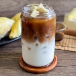 durian coffee in a glass with creamy milk and strong coffee layers, topped with fresh durian, served on ice.