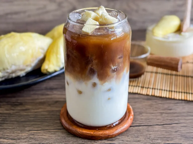 durian coffee in a glass with creamy milk and strong coffee layers, topped with fresh durian, served on ice.