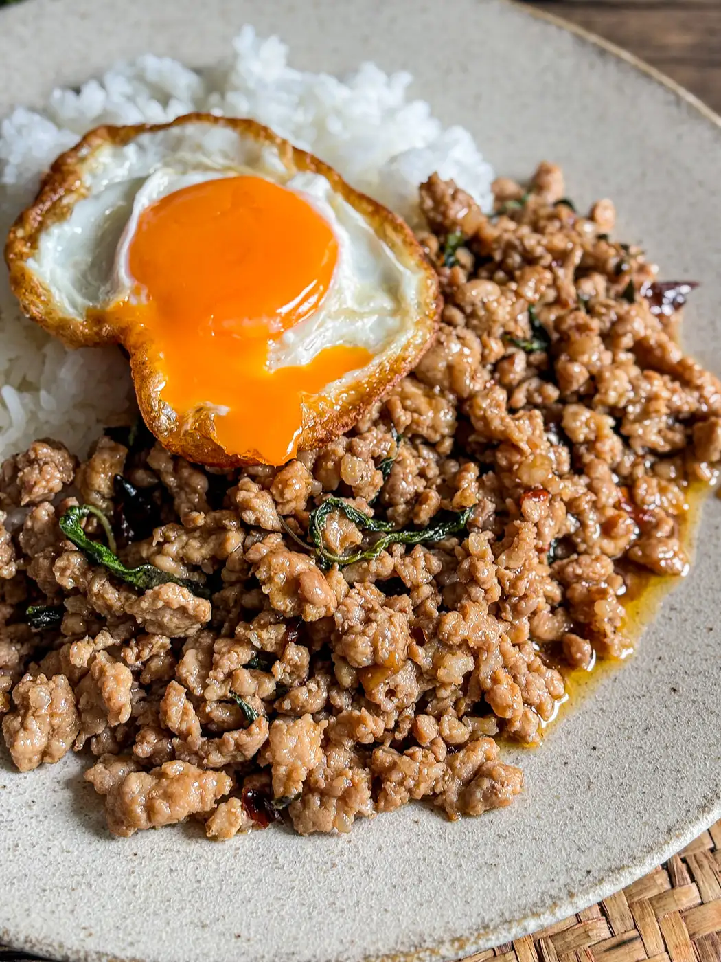 Close-up of pad krapow moo topped with a crispy fried egg and served with white rice.