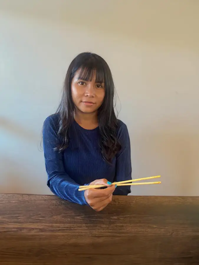 Praew with long dark hair, wearing a navy ribbed shirt, sitting indoors with soft lighting