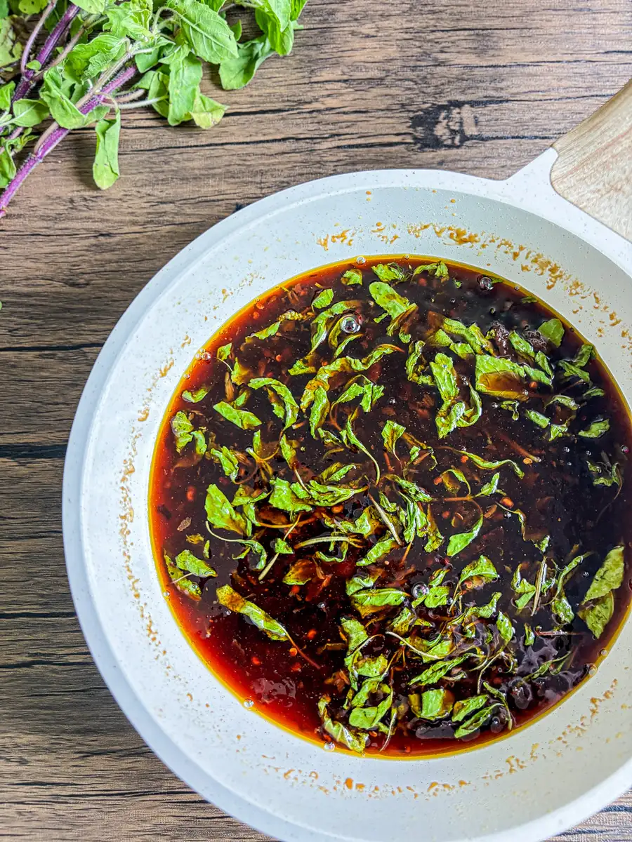 Pan of homemade Thai holy basil sauce simmering on the stove with fresh basil on top.